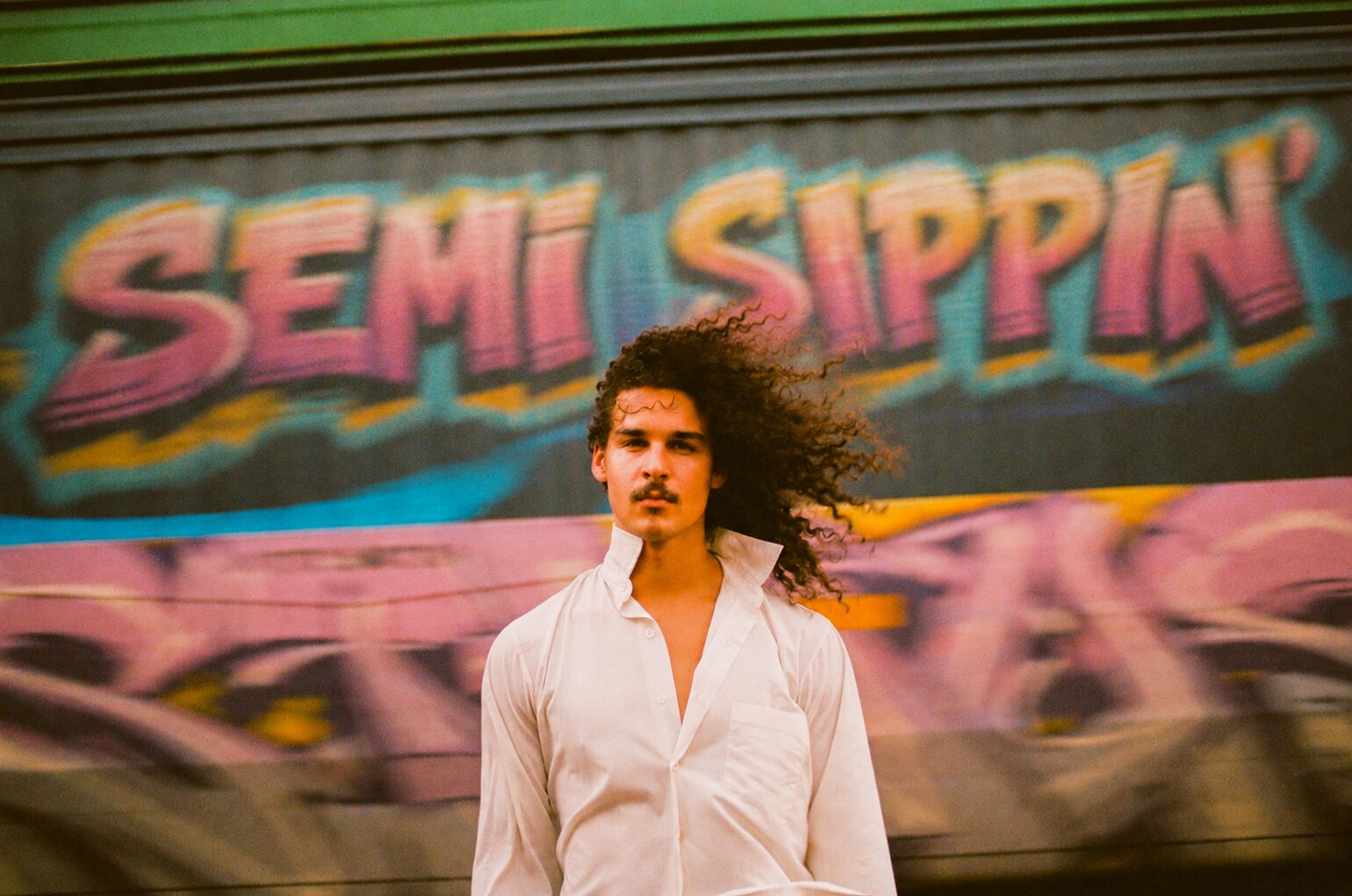 A man in a white shirt in front of a freight car painted Semi Sippin'